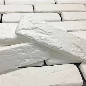 Könnte beinhalten: Weiße Ziegelwandverkleidung mit einer rauen, strukturierten Oberfläche. Die Paneele sind versetzt angeordnet und erzeugen einen rustikalen Look.