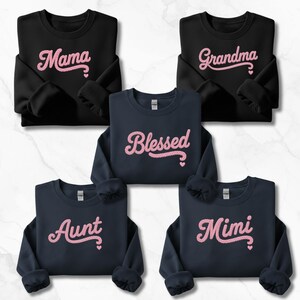 May include: Five sweatshirts in black and navy blue. Each sweatshirt has a different pink embroidered word: "Mama", "Grandma", "Blessed", "Aunt", and "Mimi". The words are in a cursive font with small heart details.