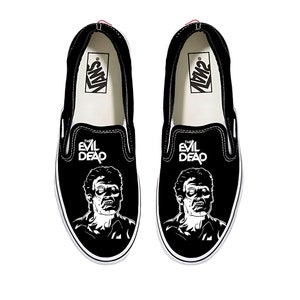 Puede incluir: Zapatillas negras sin cordones con un gráfico blanco de un zombi de la película "The Evil Dead". Las zapatillas tienen suelas blancas y el logotipo de Vans. El texto "THE EVIL DEAD" está impreso encima del gráfico del zombi.