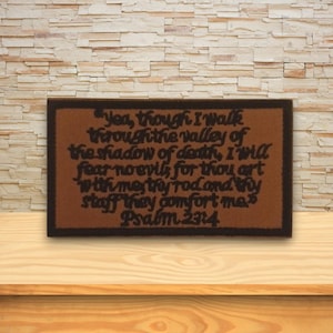 Peut inclure: Un écusson rectangulaire marron avec une bordure marron foncé. L'écusson présente un texte noir tiré du Psaume 23:4, un passage de la Bible. L'écusson est affiché sur une surface en bois contre un mur en pierre.