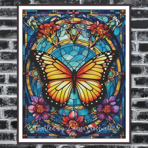 Può includere: Un'opera d'arte in vetrata incorniciata raffigurante una farfalla monarca con ali arancioni e gialle. La farfalla è centrata in un disegno circolare blu e giallo, circondata da fiori rossi e viola. Il testo "Charted by Zanna Crosswell" è in basso.