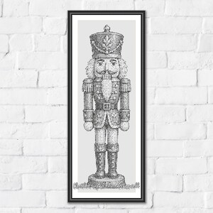 May include: A black and white cross stitch pattern featuring a detailed nutcracker soldier in a tall hat, uniform with epaulets, and tall boots. The design is framed in a thin black border and includes the text 'Christmas Nutcracker' at the bottom.