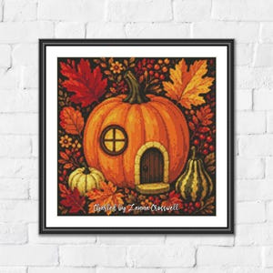 May include: A framed cross-stitch artwork featuring a large orange pumpkin house with a round window and arched door, surrounded by autumn leaves, berries, and smaller gourds. The text 'Charted by Zanna Crosswell' is printed at the bottom.