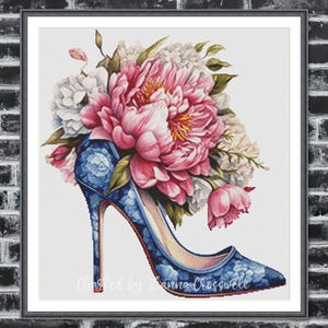 Op de afbeelding: Een ingelijst kruissteekkunstwerk met een blauwe high-heelschoen met een bloemenpatroon, overvol met roze en witte pioenrozen en andere bloemen. De tekst "Created by Anna Crosswell" is zichtbaar aan de onderkant.