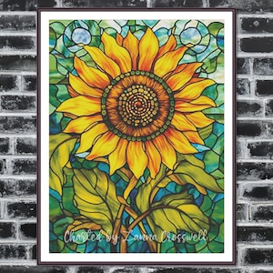 May include: A framed artwork featuring a vibrant sunflower in a stained-glass style. The sunflower has yellow petals and a brown center, set against a background of green and blue glass. The artwork is signed "Charted by Zanna Crosswell".