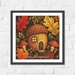 May include: A framed cross-stitch pattern featuring an acorn-shaped house with a round window and arched door, surrounded by red and yellow autumn leaves and red-capped mushrooms. The text Charted by Lanna Crosswell is printed at the bottom.