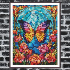 Può includere: Un'opera d'arte in vetrata incorniciata con una farfalla con ali viola, rosa e gialle. La farfalla è ambientata su uno sfondo blu con un bordo floreale di rose nei toni del rosso, arancione e rosa. Il testo "Charted by Zanna Crosswell" è in basso.