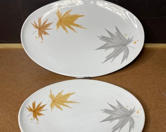 May include: Two white oval ceramic plates with a leaf design. The plates have a gray and gold leaf pattern.