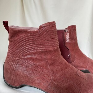 May include: A pair of burgundy leather ankle boots with a zipper on the side and the word "PUMA" printed on the side of the boot.