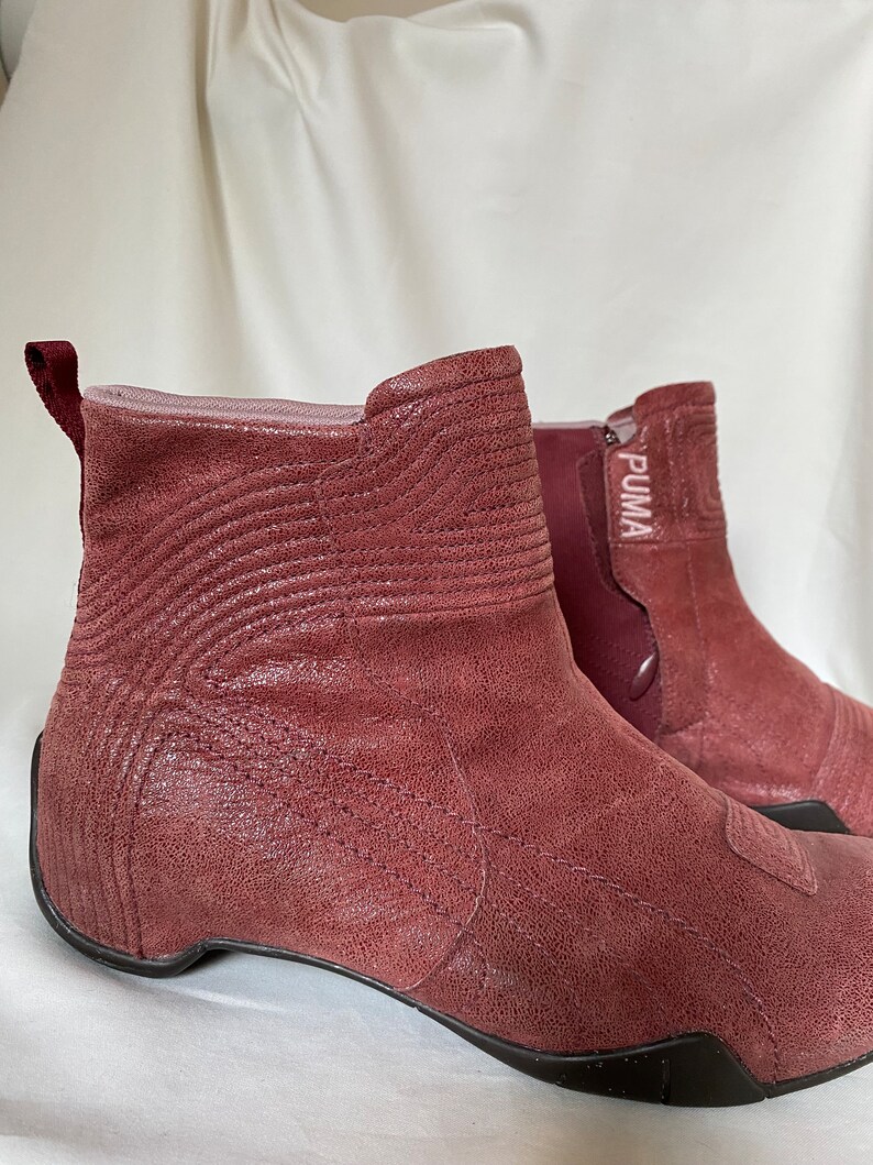 May include: A pair of burgundy leather ankle boots with a zipper on the side and the word "PUMA" printed on the side of the boot.