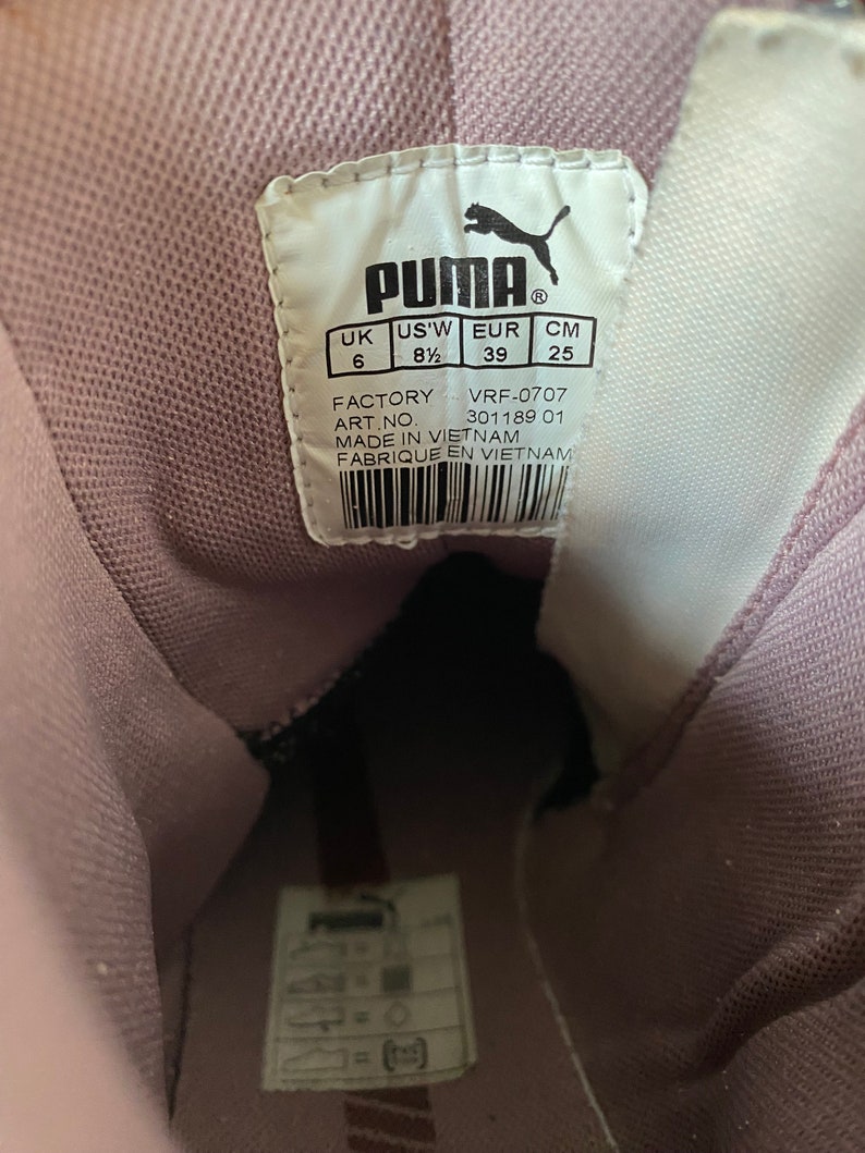 May include: A close-up of a shoe label with the Puma logo and size information. The label is white with black text and is attached to a purple shoe. The label reads: UK 6, US'W 8 1/2, EUR 39, CM 25. The label also includes the factory code VRF-0707, the article number 301189 01, and the words "Made in Vietnam" and "Fabrique en Vietnam".