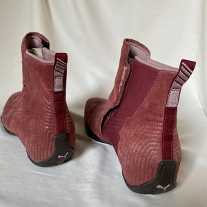 May include: A pair of burgundy suede ankle boots with a black rubber sole. The boots have a zipper on the inside of the ankle and a pull tab on the back.