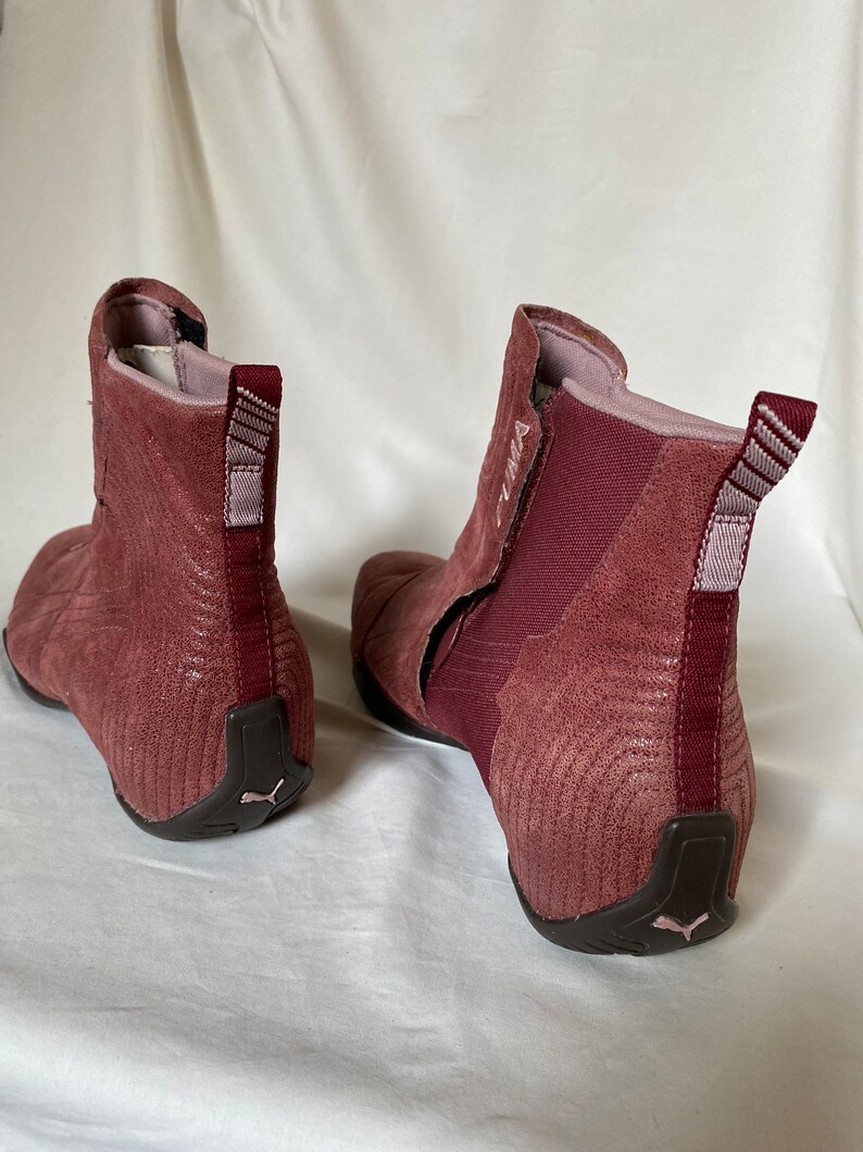 May include: A pair of burgundy suede ankle boots with a black rubber sole. The boots have a zipper on the inside of the ankle and a pull tab on the back.