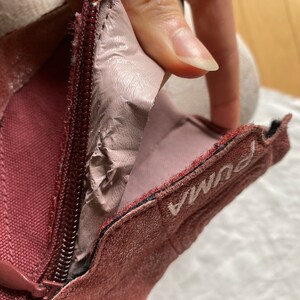 May include: Close-up of a burgundy suede boot with a zipper and the word "Puma" embroidered on the side.