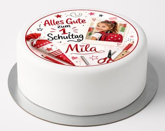 May include: A round white cake featuring a printed design with the text Alles Gute zum 1. Schultag Mila, a red and white star-patterned school cone, a photograph of a child with a backpack, a red pencil, a spiral notebook, and red scissors.