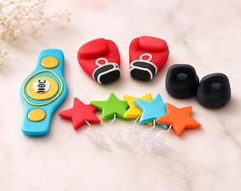 May include: A set of decorative fondant cake toppers featuring a blue and yellow championship belt with the text 18C, two red boxing gloves with black and white cuffs, two black kettlebells, and five colorful stars with white curly wire accents.
