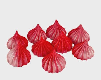 May include: A collection of nine conical, ridged meringue cookies arranged in a cluster. Each cookie features a vibrant red color that transitions into a lighter, frosted pink hue at the base, with a distinct pointed top and a fluted, star-shaped edge.