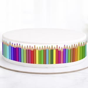 Könnte beinhalten: Ein runder, weißer Kuchen, verziert mit einem bunten Bleistift-Rand. Die Bleistifte sind in einer Reihe angeordnet und zeigen ein Farbspektrum. Der Kuchen steht auf einer weißen Kuchenplatte, perfekt für einen Geburtstag oder eine Feier.