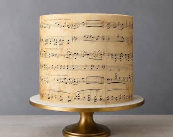 May include: A cylindrical cake with a cream-colored surface featuring a printed black musical score and aged paper texture. The cake rests on a circular white marble platform supported by a metallic gold pedestal stand with a wide base.