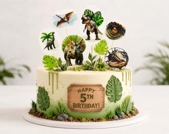 May include: A round cake with white and green ombre frosting, decorated with green fondant monstera leaves and a wooden-style plaque reading HAPPY 5TH BIRTHDAY. The top features various dinosaur-themed paper toppers and a central triceratops figure.