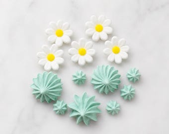 May include: Five white daisy-shaped sugar decorations with bright yellow centers arranged at the top, accompanied by nine pale mint green piped meringue-style swirls of varying sizes arranged in a cluster below the flowers.