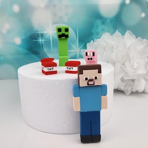Könnte beinhalten: Ein Minecraft-Tortenaufleger-Set mit einem grünen Creeper, einem rosa Schwein, zwei roten TNT-Blöcken und einer blauen und braunen Steve-Figur.