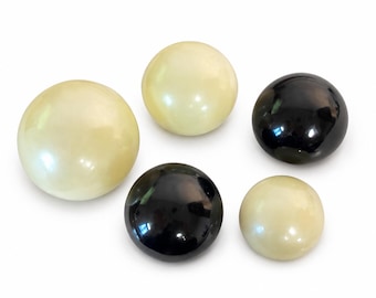 May include: A collection of five smooth, spherical objects of varying sizes. Three of the spheres are a creamy off-white color, while the other two are a glossy, solid black. Each sphere features a polished, reflective surface finish.