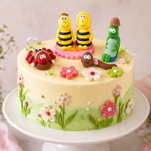 Könnte beinhalten: Ein runder Kuchen mit hellgelber Glasur, verziert mit grünem Zuckerguss-Gras und bunten Fondantblumen. Obenauf befinden sich Fondantfiguren, darunter zwei gelb-schwarz gestreifte Bienen, ein roter Marienkäfer, ein brauner Wurm und eine grüne Raupe.