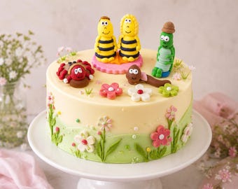 May include: A round cake with pale yellow frosting, decorated with green icing grass and colorful fondant flowers. Topped with fondant figures including two yellow and black striped bees, a red ladybug, a brown worm, and a green caterpillar.