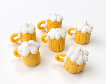 May include: Six miniature beer mug figurines crafted from yellow material with textured vertical lines on the sides and a white, rounded, cloud-like foam topping. Each mug features a small, curved handle extending from the side of the vessel.