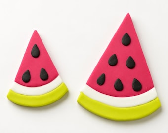 May include: Two triangular watermelon slice decorations in different sizes. Each piece features a bright pink fruit section with black teardrop-shaped seeds, a thin white rind layer, and a thicker lime green outer rind edge on a plain background.