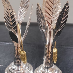May include: Two silver palm tree candle holders with gold accents. The candle holders are made of metal and have a detailed design.