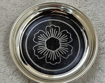 May include: Silver coaster with a decorative flower design in the center.