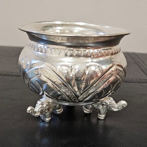 May include: A silver bowl with an ornate design and three elephant legs.