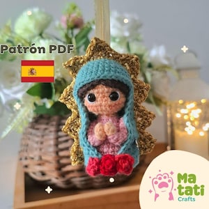 Op de afbeelding: Gehaakte pop van de Maagd Maria, met een blauwe sluier, roze gewaad en rode rozen, tegen een gouden sterrenachtergrond. De afbeelding bevat de tekst "Patrón PDF" en een Spaanse vlag. Handgemaakt.