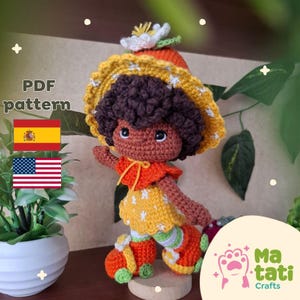 Puede incluir: Muñeca de ganchillo hecha a mano con un atuendo amarillo y naranja, un sombrero a juego y cabello castaño rizado. La muñeca tiene una expresión alegre y está de pie. La imagen incluye el texto "PDF pattern" y las banderas de España y Estados Unidos.