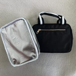 May include: Two insulated lunch bags. One is silver with a white zipper and the other is black with a gold zipper and white handles.