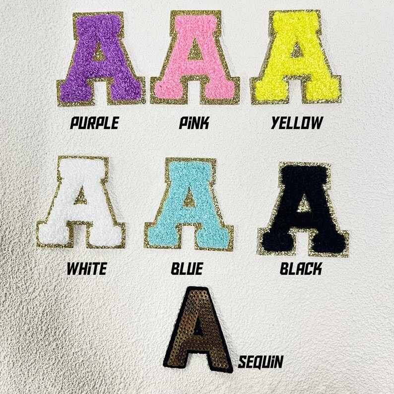 May include: Six iron-on patches in different colors and textures, each featuring a large capital letter "A". The colors are purple, pink, yellow, white, blue, and black. The last patch is gold and has a sequin texture. The patches are labeled with their colors below.