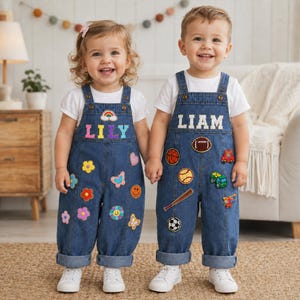 Könnte beinhalten: Zwei blaue Jeans-Latzhosen über weißen T-Shirts. Das linke Modell zeigt den Namen LILY, einen Regenbogen, Blumen, einen Schmetterling und ein Herz. Das rechte Modell zeigt den Namen LIAM, einen Football, Basketball, Baseball, Schläger, Fußball, LKW und Hubschrauber als Aufnäher.