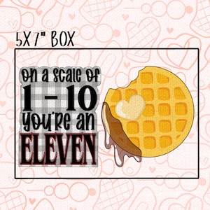 Puede incluir: Caja rectangular con el texto "5x7" BOX" en la parte superior. La imagen presenta un gofre con un mordisco, cubierto con una nuez de mantequilla. El texto a la izquierda dice "on a scale of 1-10 you're an ELEVEN" en un diseño a cuadros.