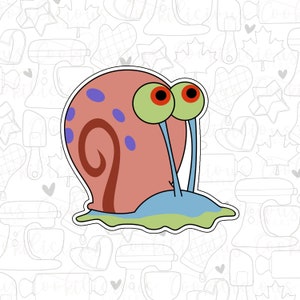 Puede incluir: Un caracol de dibujos animados con una concha rosa, una espiral marrón, un cuerpo azul y ojos grandes verdes con pupilas rojas. El caracol está sobre un fondo blanco con un patrón de utensilios de cocina y corazones.