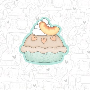 Könnte beinhalten: Ein hellbrauner Kuchen mit einer hellblauen Kruste und einem weißen Schlagsahne-Topping mit einem Pfirsichstück obenauf. Der Kuchen hat drei rote Herzen obenauf.