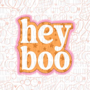May include: A pink and orange cookie cutter with the text "hey boo" in white letters. The cutter is decorated with a pattern of orange stars.
