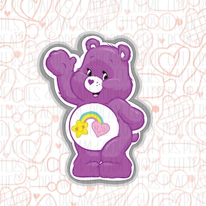 May include: Purple Care Bear cookie cutter with a rainbow and a yellow star on its belly. The Care Bear is waving with a friendly smile.