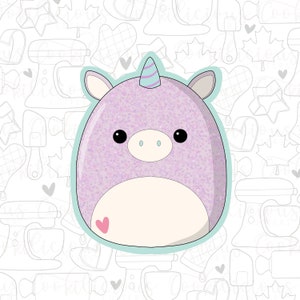 May include: A purple and white unicorn-shaped plush toy with a blue horn and a pink heart on its belly. The toy is surrounded by a light blue outline.