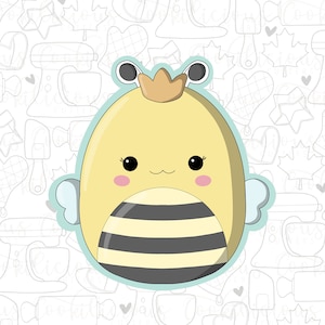 Op de afbeelding: Een schattige cartoon-bij met een geel lichaam, zwarte strepen en een gouden kroon. De bij heeft grote, zwarte ogen en roze wangen. De bij is omringd door een lichtblauwe omtrek.