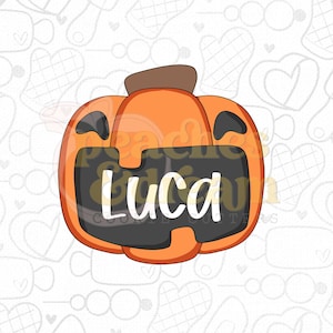 May include: An orange pumpkin-shaped cookie cutter with a brown stem and a large black rectangular center area featuring the name Luca written in white script. The design includes two black curved eye shapes at the top of the pumpkin.