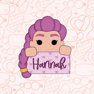 May include: A cartoon illustration of a person with purple hair holding a sign that says "Hannah". The sign is light purple with small heart patterns. The background is a light pink color with heart and oven mitt patterns.