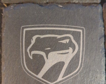 May include: A black slate coaster with a white engraved Dodge Viper logo. The logo features a snake's head with a raised hood and the text "2013-Present".