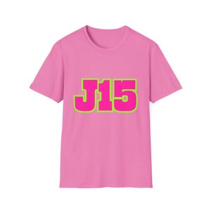 May include: A pink t-shirt with the text "J15" in a bold, neon green outline. The shirt is a short-sleeved crew neck style, and the text is centered on the front.